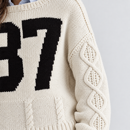Close-up of the cable knit sleeve and black 87 on the cream sweater
